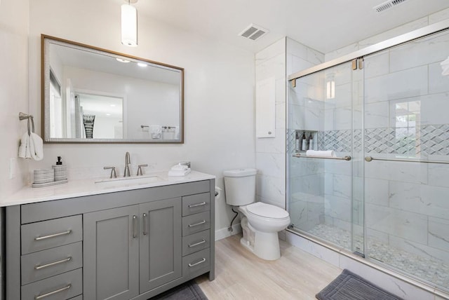 bathroom with hardwood / wood-style floors, vanity, a shower with door, and toilet