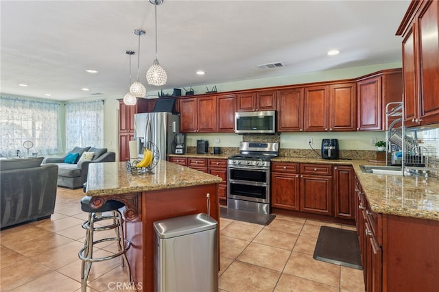 kitchen with light tile patterned floors, a kitchen island, decorative light fixtures, appliances with stainless steel finishes, and a kitchen breakfast bar