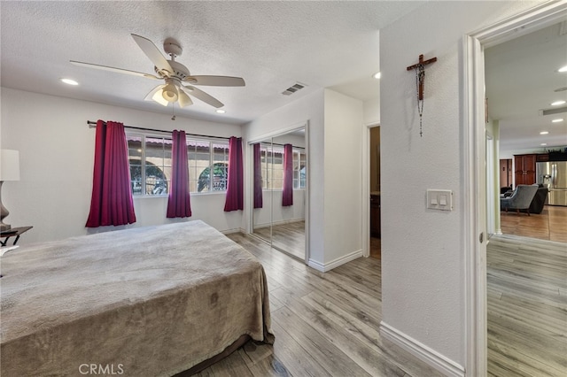 bedroom featuring ceiling fan, a textured ceiling, stainless steel refrigerator with ice dispenser, a closet, and light wood-type flooring