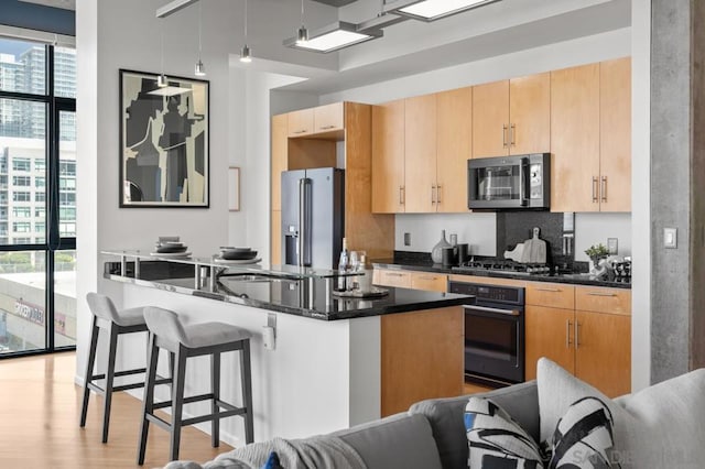 kitchen with black appliances, light wood-type flooring, light brown cabinets, and a breakfast bar area