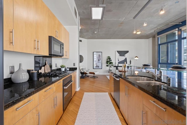 kitchen featuring light brown cabinets, light wood-type flooring, dark stone countertops, black appliances, and sink