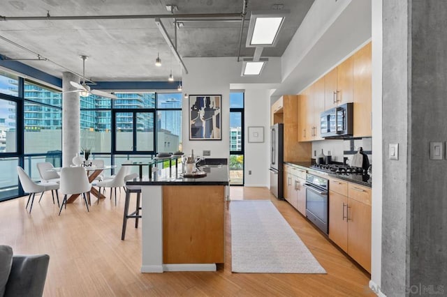 kitchen with stainless steel appliances, a kitchen island, a kitchen breakfast bar, a wealth of natural light, and light hardwood / wood-style flooring