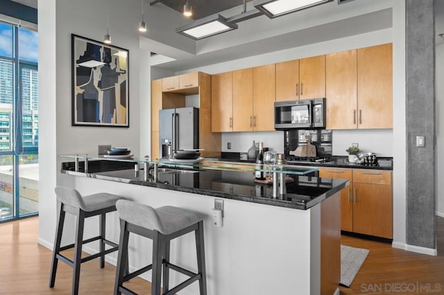 kitchen with hardwood / wood-style floors, kitchen peninsula, high end refrigerator, a kitchen breakfast bar, and dark stone countertops