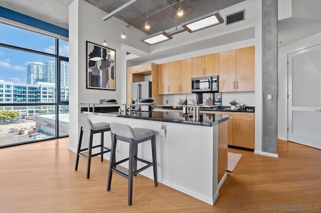 kitchen with kitchen peninsula, light wood-type flooring, appliances with stainless steel finishes, light brown cabinets, and dark stone counters