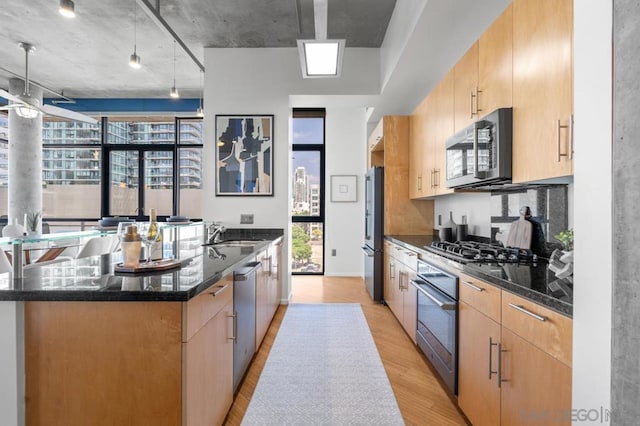 kitchen with a large island, light wood-type flooring, stainless steel appliances, and dark stone countertops