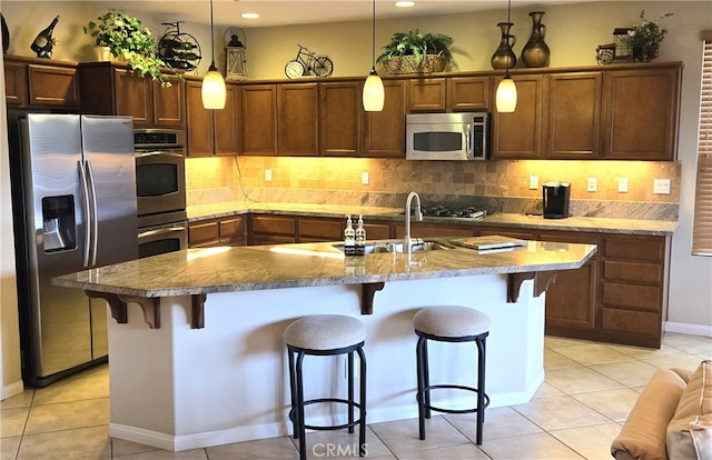 kitchen with appliances with stainless steel finishes, a breakfast bar, an island with sink, and decorative light fixtures