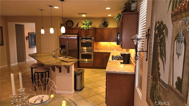 kitchen with sink, a kitchen bar, decorative light fixtures, light tile patterned floors, and appliances with stainless steel finishes