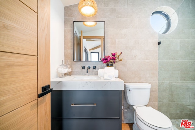 bathroom featuring tile walls, vaulted ceiling, backsplash, vanity, and toilet