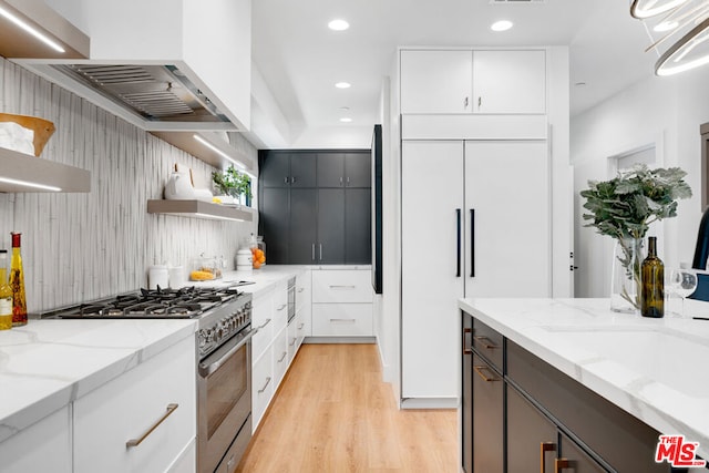 kitchen with light hardwood / wood-style floors, stainless steel gas range oven, light stone counters, and white cabinetry