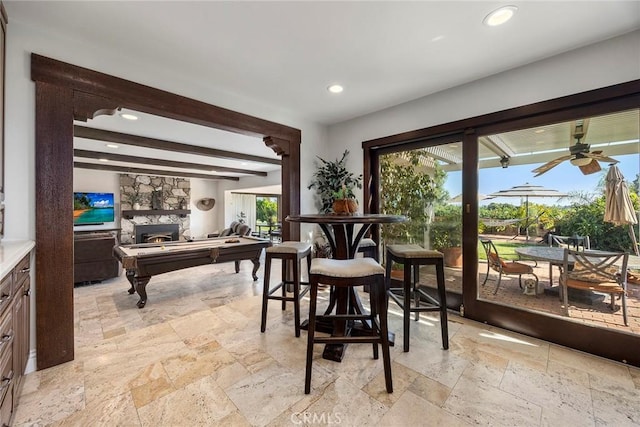 dining space with a stone fireplace, ceiling fan, plenty of natural light, and beamed ceiling