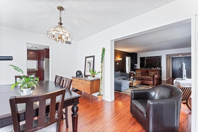 dining room with a notable chandelier, wood-type flooring, and a textured ceiling