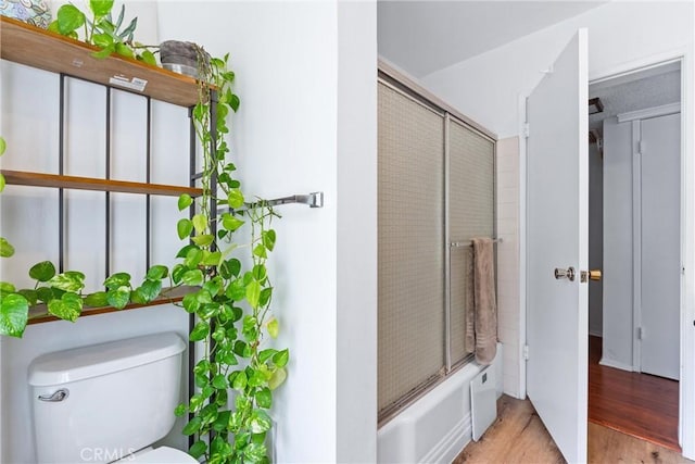 bathroom featuring hardwood / wood-style floors, toilet, and combined bath / shower with glass door