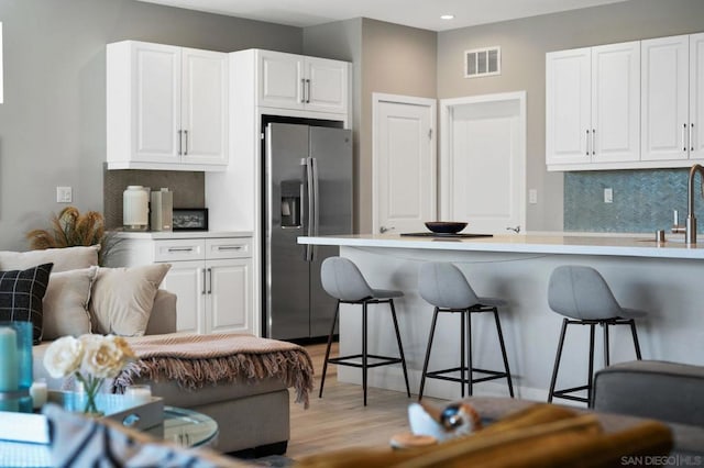 kitchen with stainless steel fridge with ice dispenser, white cabinets, a kitchen breakfast bar, light hardwood / wood-style flooring, and backsplash