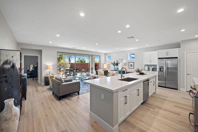 kitchen featuring appliances with stainless steel finishes, light hardwood / wood-style floors, an island with sink, white cabinets, and sink