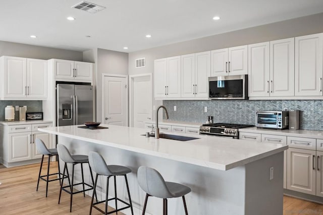 kitchen with a kitchen breakfast bar, an island with sink, white cabinetry, and stainless steel appliances