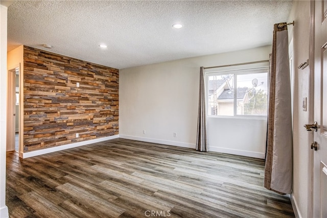 unfurnished room with wood walls, a textured ceiling, and dark hardwood / wood-style floors