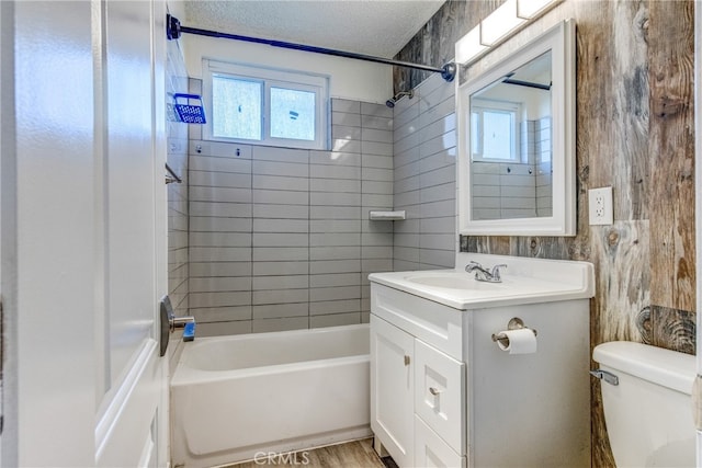 full bathroom featuring a textured ceiling, tiled shower / bath, vanity, and toilet