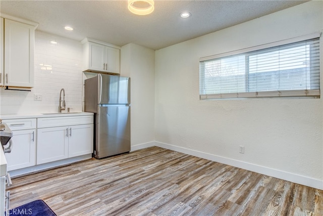 kitchen with light hardwood / wood-style floors, a textured ceiling, sink, white cabinets, and stainless steel refrigerator