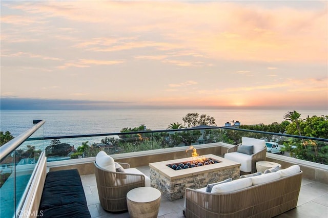 balcony at dusk featuring a water view and an outdoor living space with a fire pit