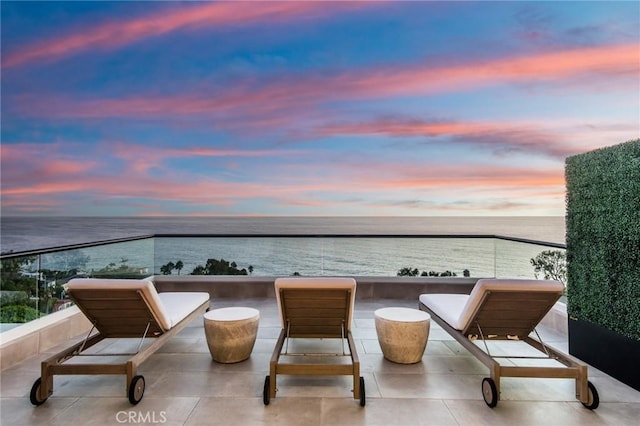 balcony at dusk featuring a water view