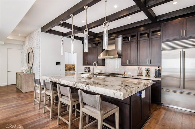 kitchen with a large island with sink, dark hardwood / wood-style flooring, light stone counters, dark brown cabinetry, and stainless steel appliances