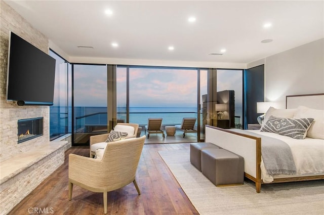 bedroom featuring hardwood / wood-style floors, a water view, a stone fireplace, and expansive windows