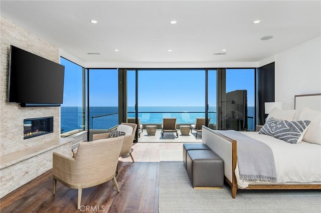 bedroom with a fireplace, a water view, wood-type flooring, and a wall of windows