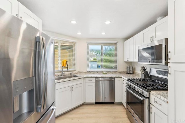 kitchen with appliances with stainless steel finishes, light hardwood / wood-style floors, light stone counters, and white cabinets