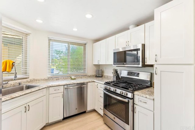 kitchen featuring white cabinets, appliances with stainless steel finishes, light hardwood / wood-style floors, and light stone countertops