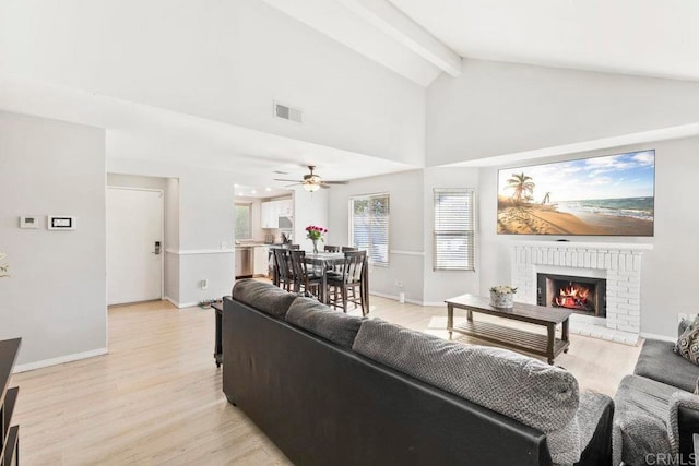 living room with light hardwood / wood-style flooring, a brick fireplace, vaulted ceiling with beams, and ceiling fan