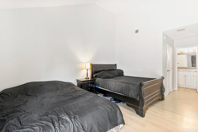 bedroom featuring light hardwood / wood-style floors, connected bathroom, and lofted ceiling