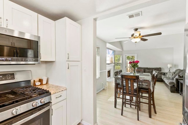 kitchen with ceiling fan, white cabinets, lofted ceiling, appliances with stainless steel finishes, and light wood-type flooring