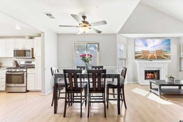 dining room with light hardwood / wood-style flooring, a brick fireplace, vaulted ceiling, and ceiling fan