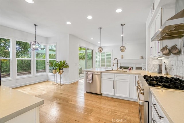 kitchen with pendant lighting, white cabinetry, wall chimney range hood, and appliances with stainless steel finishes