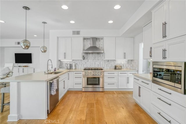 kitchen with sink, wall chimney range hood, kitchen peninsula, decorative light fixtures, and appliances with stainless steel finishes