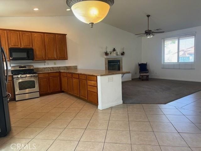 kitchen featuring a peninsula, open floor plan, black appliances, brown cabinetry, and a glass covered fireplace