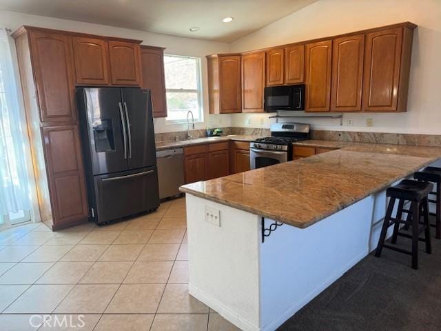 kitchen featuring a peninsula, a kitchen bar, appliances with stainless steel finishes, and light tile patterned flooring