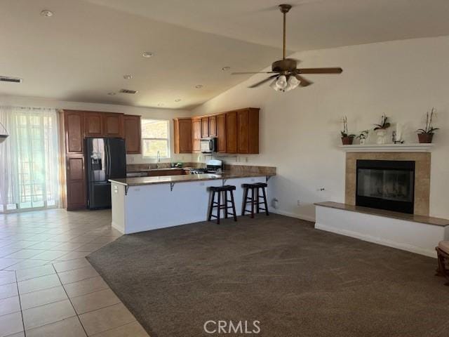 kitchen with brown cabinets, dark countertops, stainless steel fridge, and a peninsula