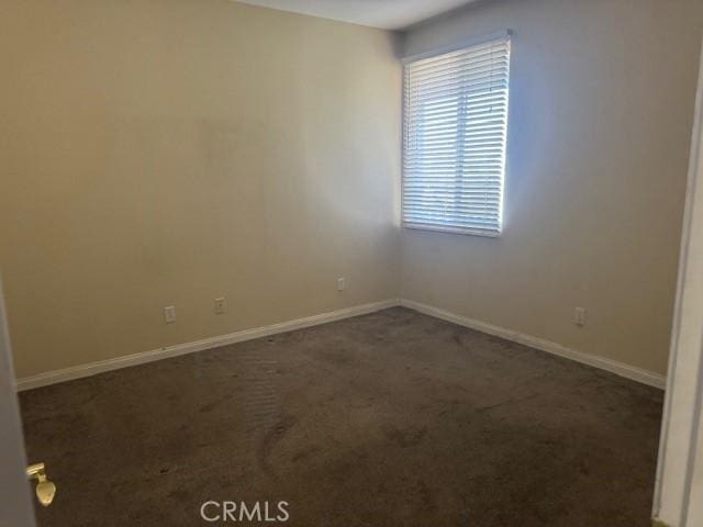 spare room featuring baseboards and dark colored carpet