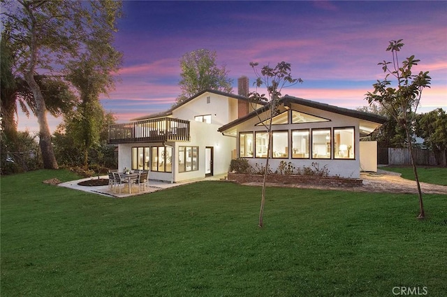 back house at dusk featuring a yard, a balcony, a patio area, and a sunroom