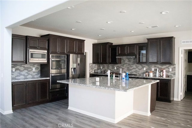 kitchen featuring an island with sink, backsplash, appliances with stainless steel finishes, and light hardwood / wood-style flooring