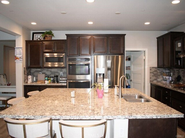 kitchen with appliances with stainless steel finishes, tasteful backsplash, a large island, a kitchen bar, and sink