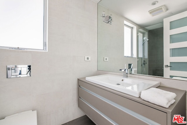 bathroom featuring a shower, vanity, a wealth of natural light, and tile walls