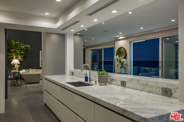 kitchen with light stone counters, sink, white cabinets, and a spacious island