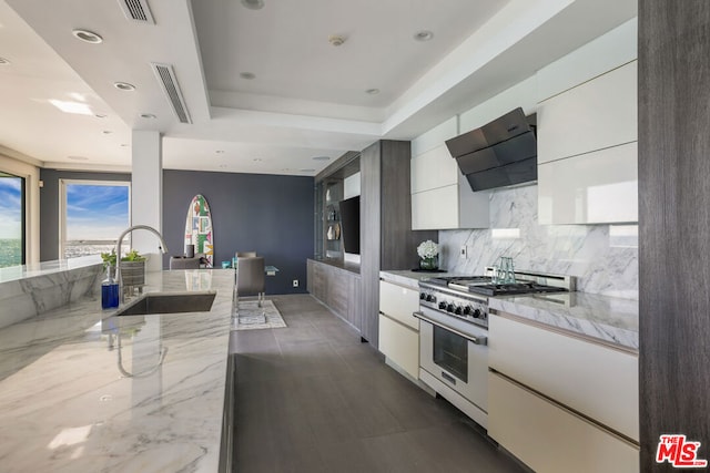 kitchen featuring sink, high end range, light stone counters, range hood, and white cabinets