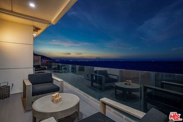 balcony at dusk featuring a water view