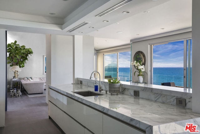 kitchen featuring white cabinets, light stone countertops, sink, and a water view