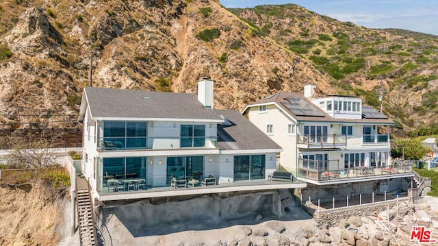 back of property with a mountain view and solar panels