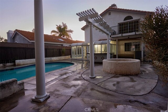 pool at dusk featuring a patio area and a sunroom