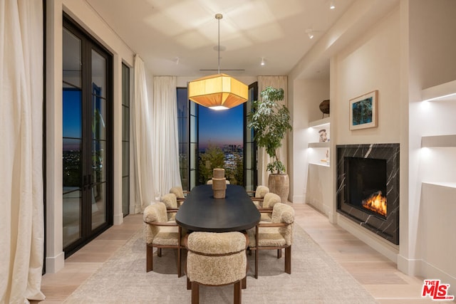 dining room with light wood-type flooring, french doors, and a fireplace